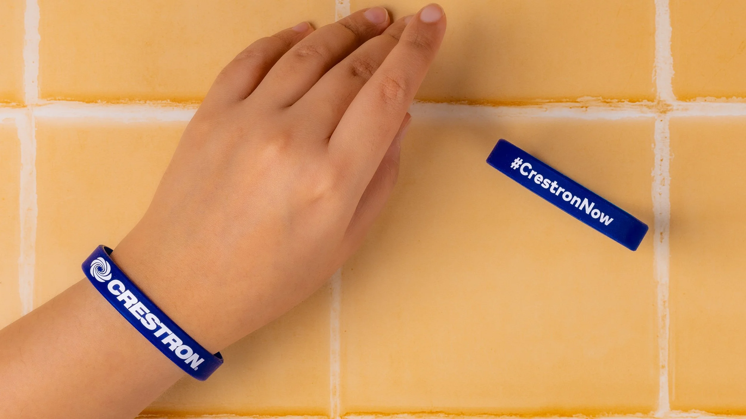 Navy Crestron silicone wristband worn on a wrist, with a second band flat showing the #CrestronNow hashtag