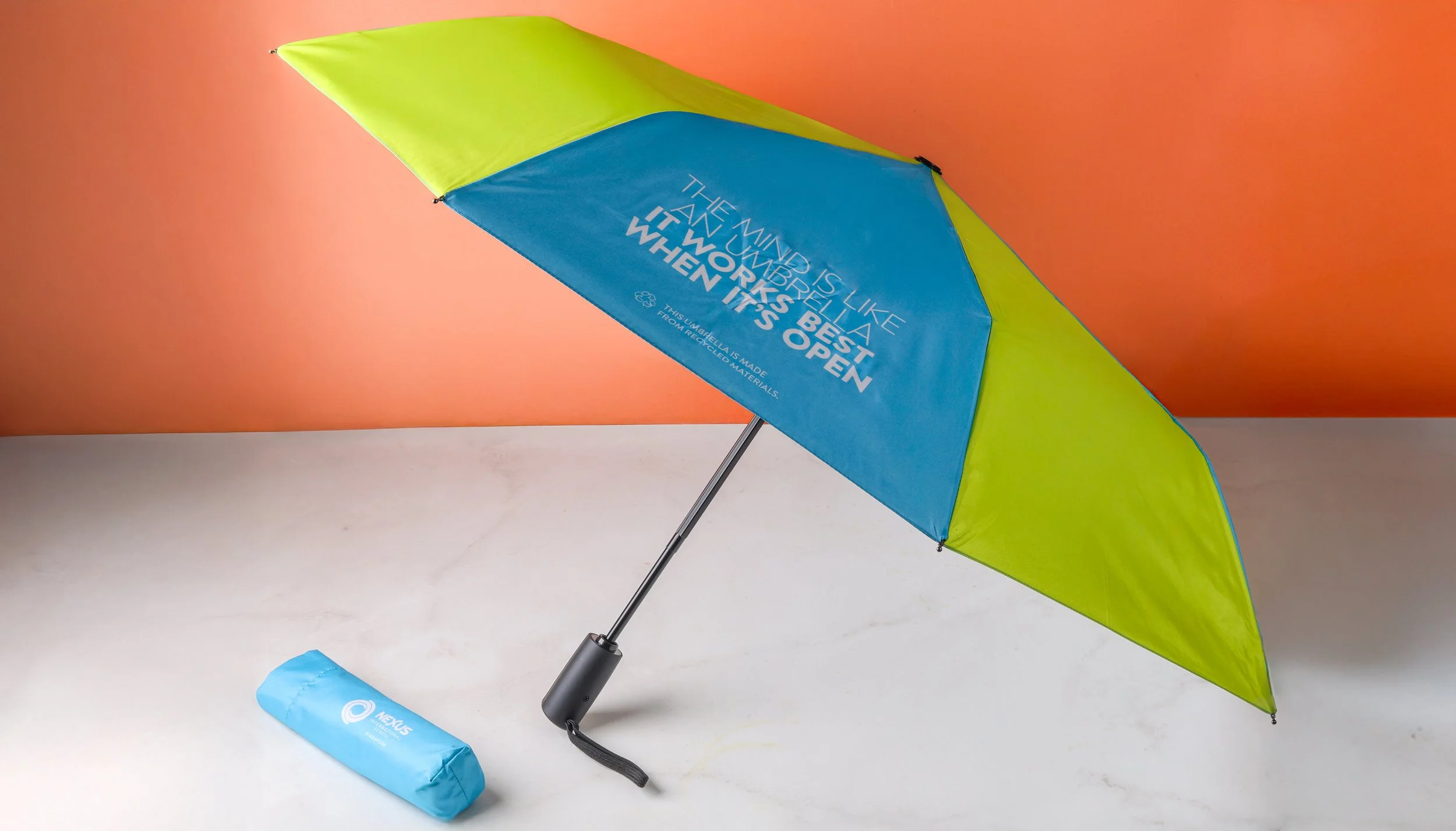 Nexus International School custom umbrella in lime and teal, printed with a slogan and made from recycled materials