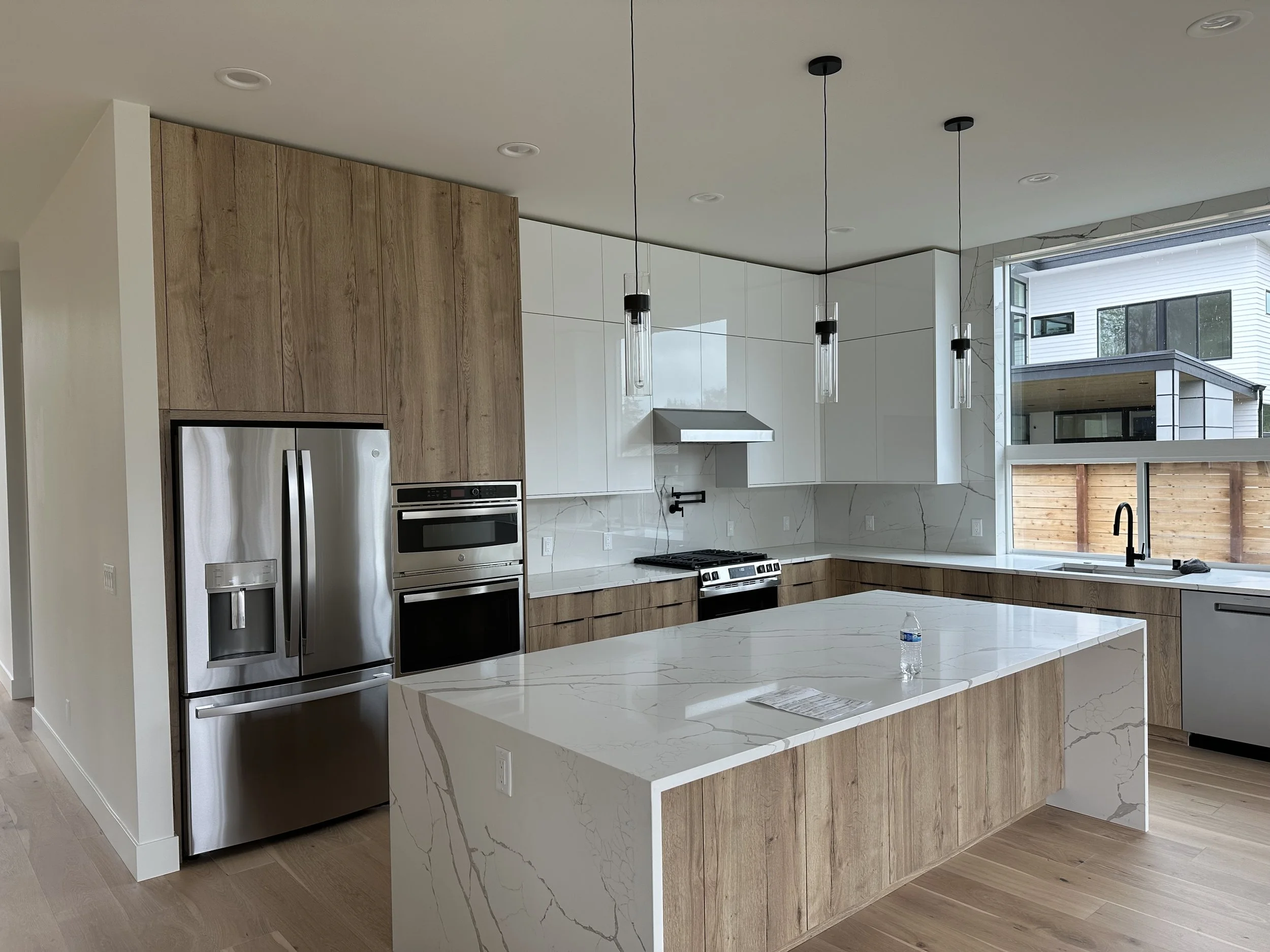 Modern kitchen with white cabinets, wooden accents, stainless steel refrigerator, and a large marble island.