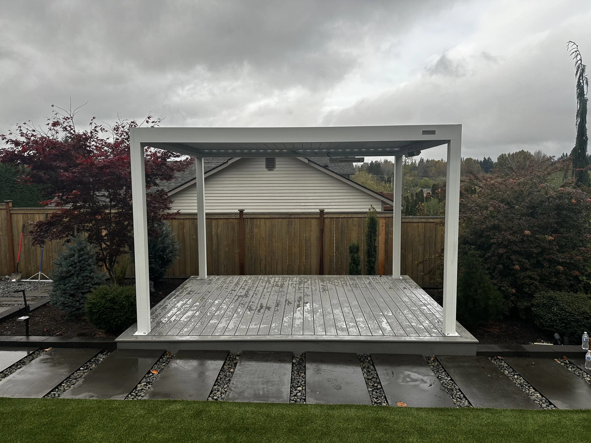Backyard with deck, pergola, trees, and cloudy sky.