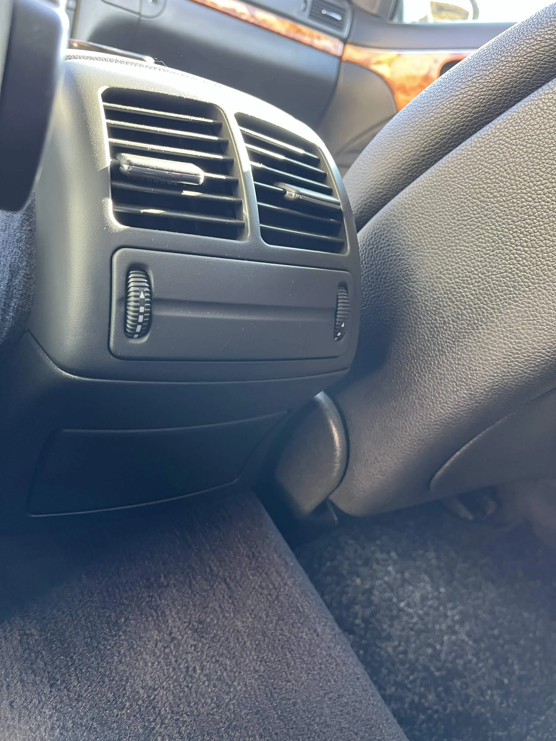 Close-up of vehicle dashboard air vent and part of driver's side interior with leather armrest.