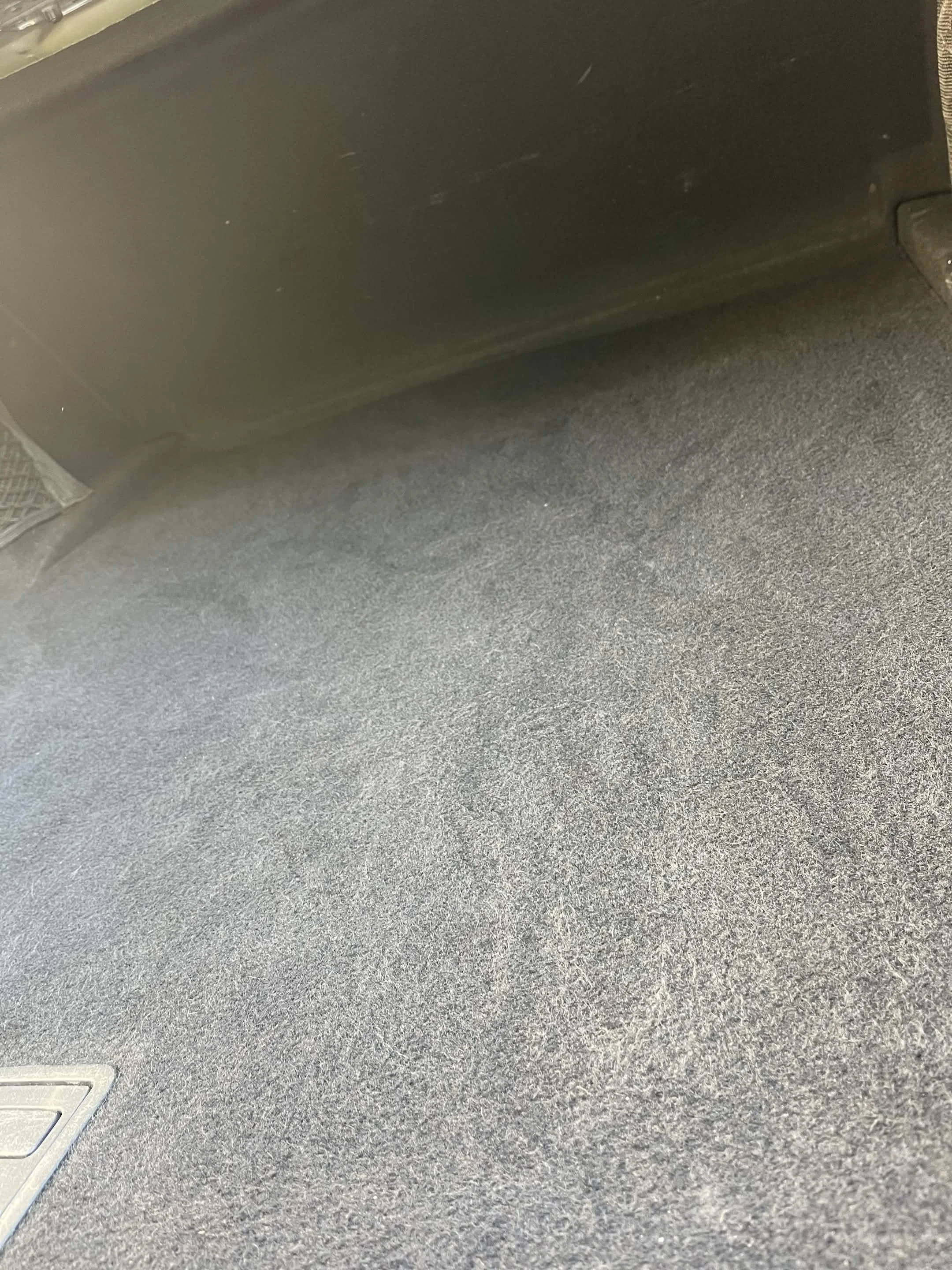 Carpeted floor of a vehicle interior with a floor drain cover visible in the lower left corner.