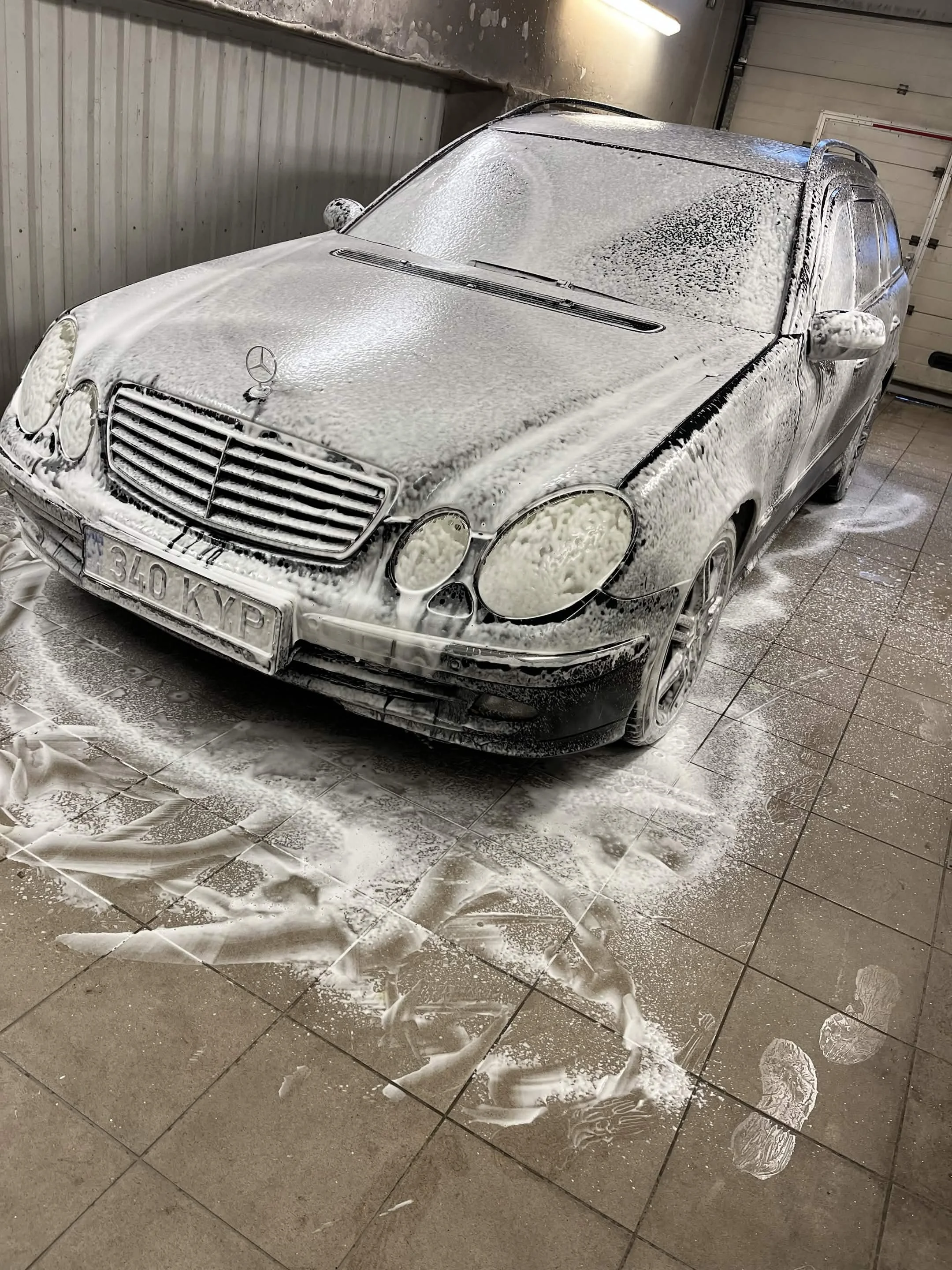 Garaažis seisab seebivahtuga kaetud must Mercedes-Benz, mille keraamilisel põrandal on seebiplekke.