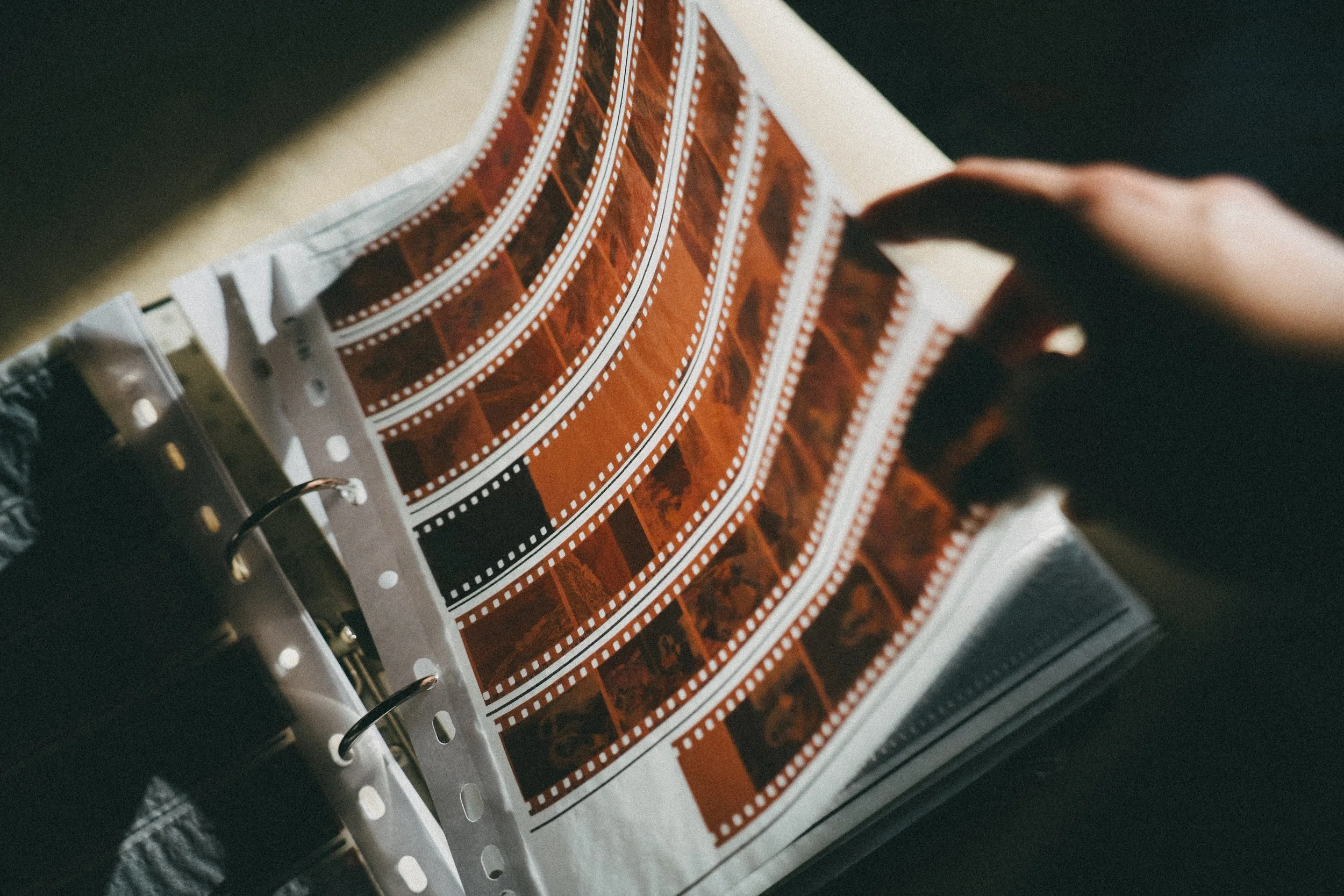 Una mano che sfoglia un quaderno con fogli di film fotografici di colore marrone e bianco.
