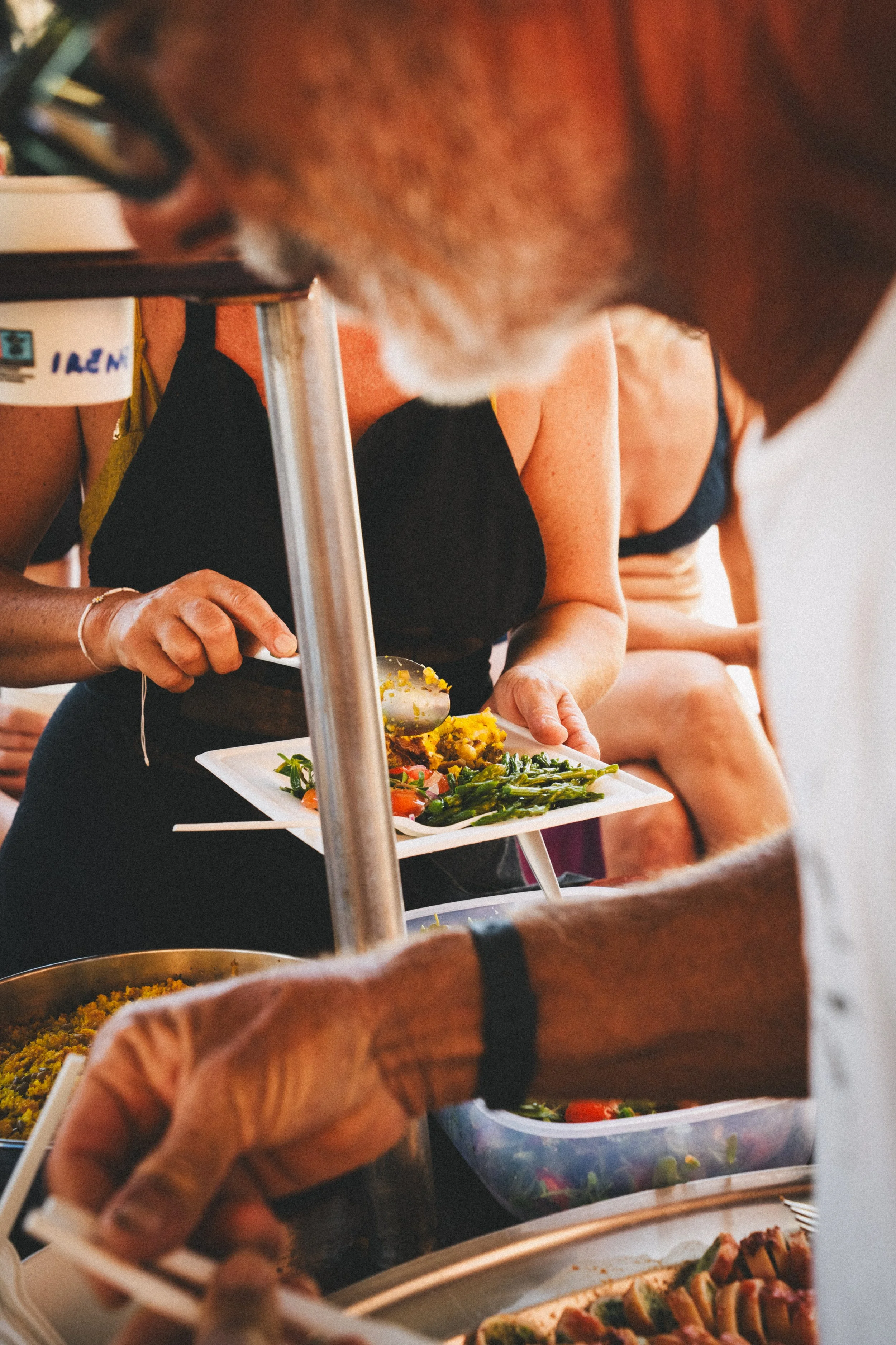 Persone che servono cibo al buffet con piatti di verdure e riso, in un contesto di ristorazione informale.
