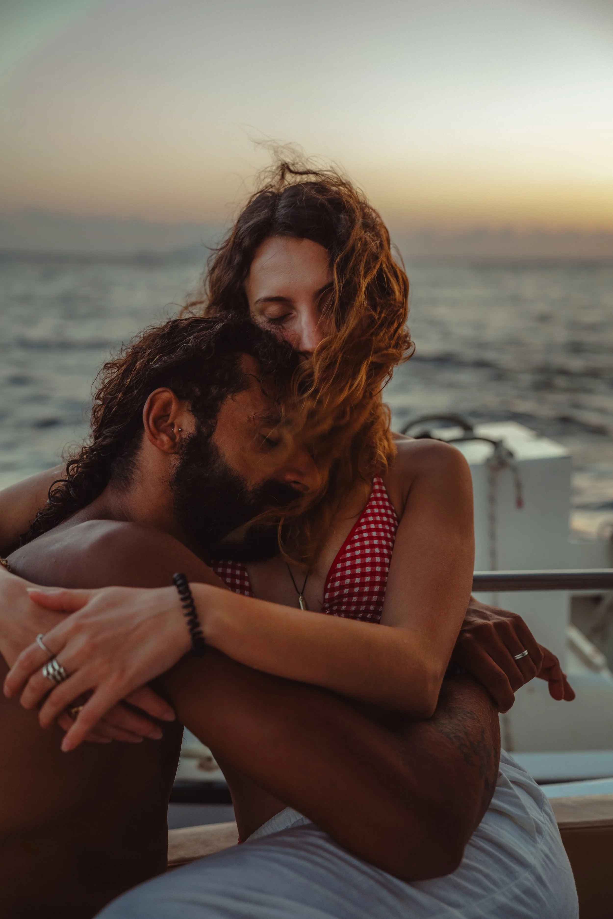 Una coppia si abbraccia affettuosamente su una barca mentre il sole tramonta sul mare.