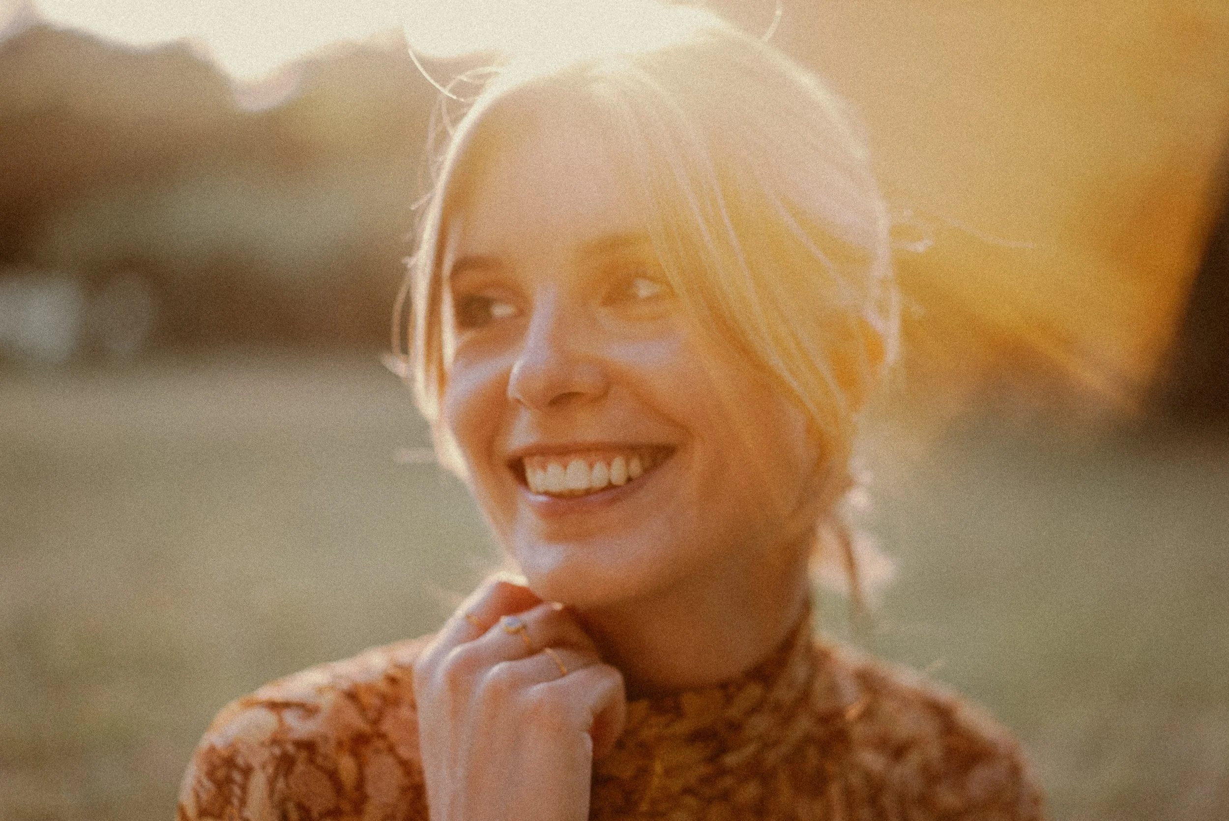 Una donna sorridente con i capelli biondi chiari, indossa un vestito con motivo floreale arancione e ha un sorriso felice.