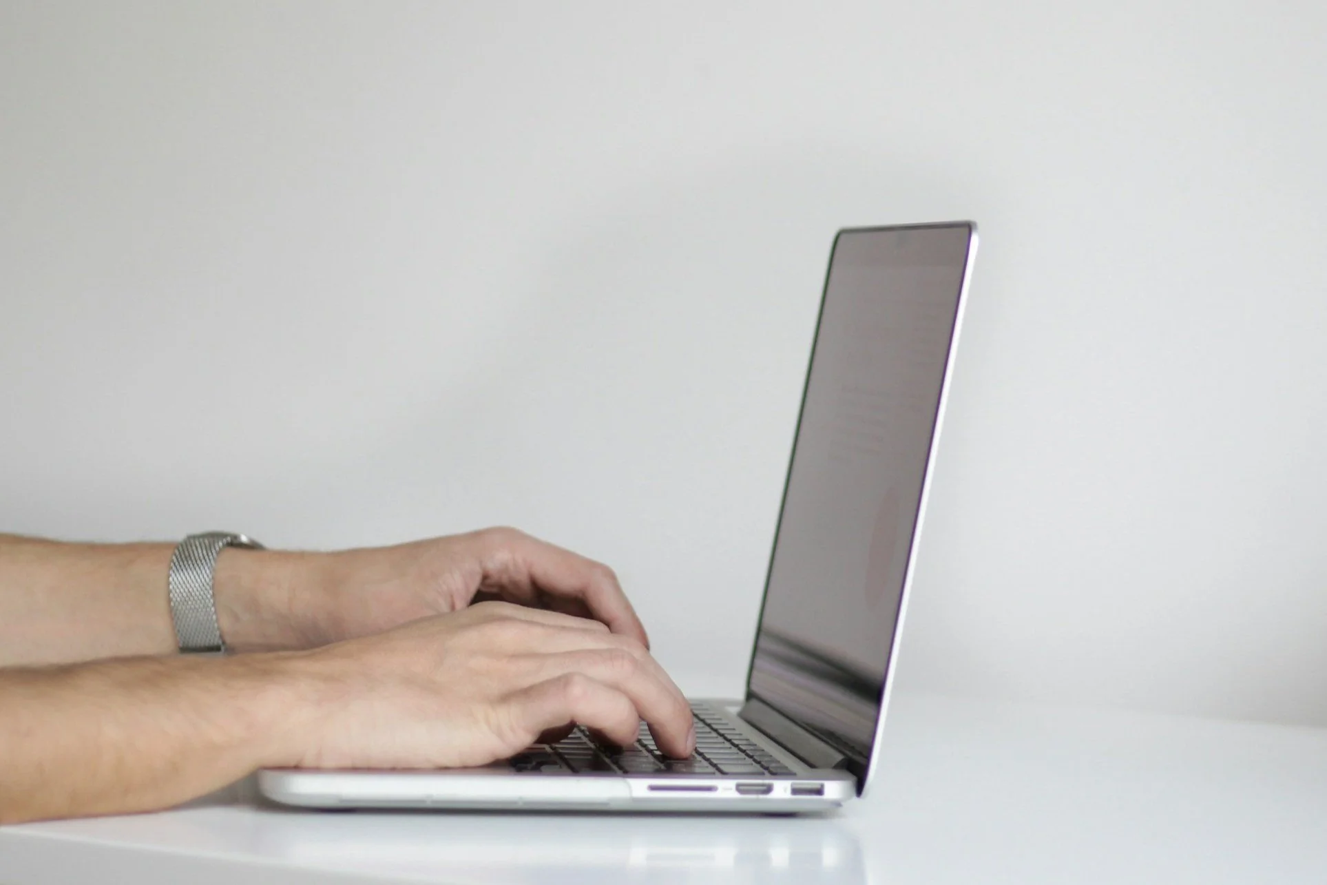 Person typing on a silver laptop with a white background.
