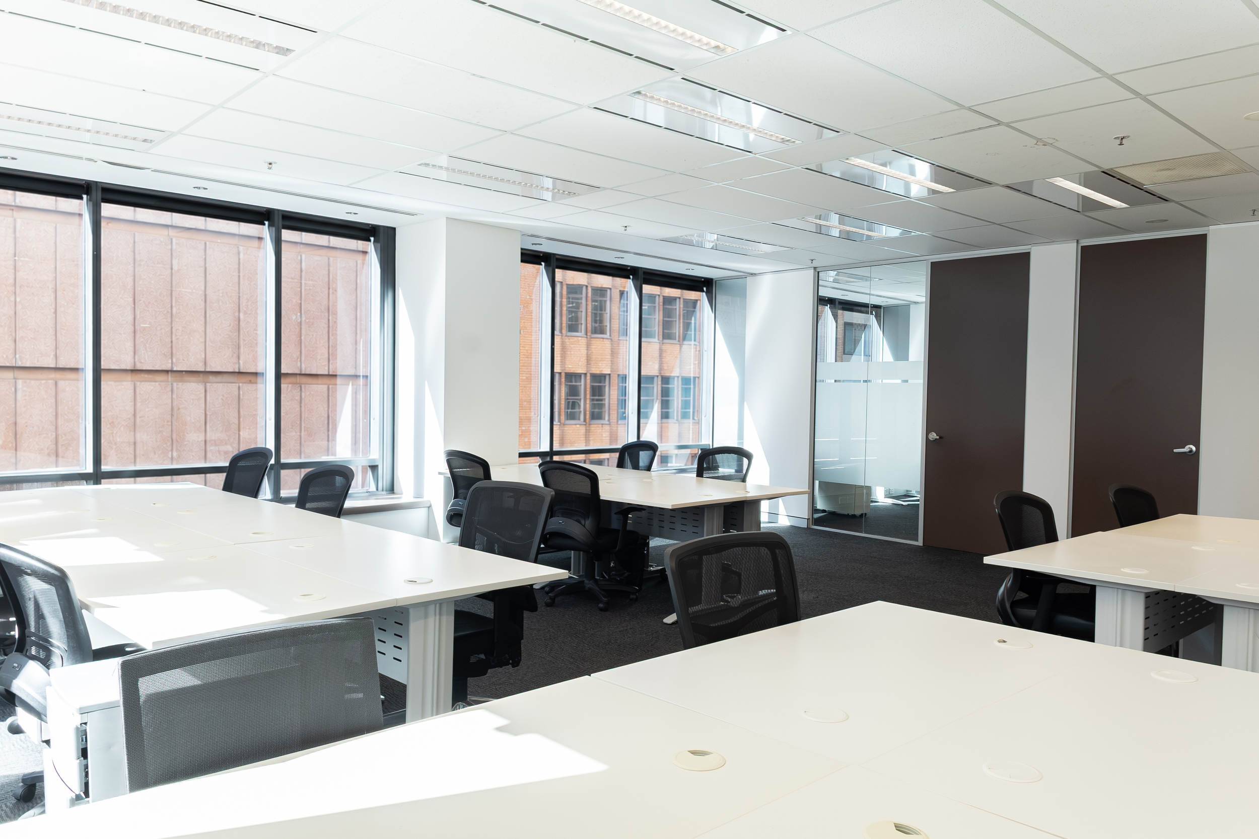 Modern office conference room with white tables, black mesh chairs, large windows, and a city view.