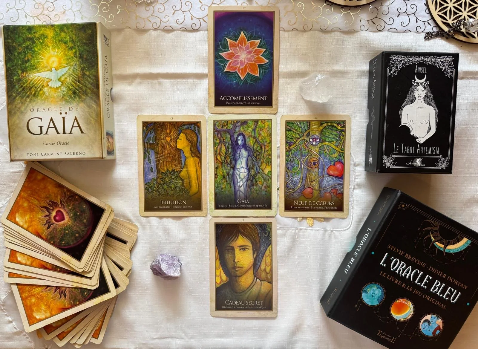 Jeu de cartes de tarot et livres liés à l'oracle et à la divination, avec pierres et cristaux, présentés sur une nappe blanche.