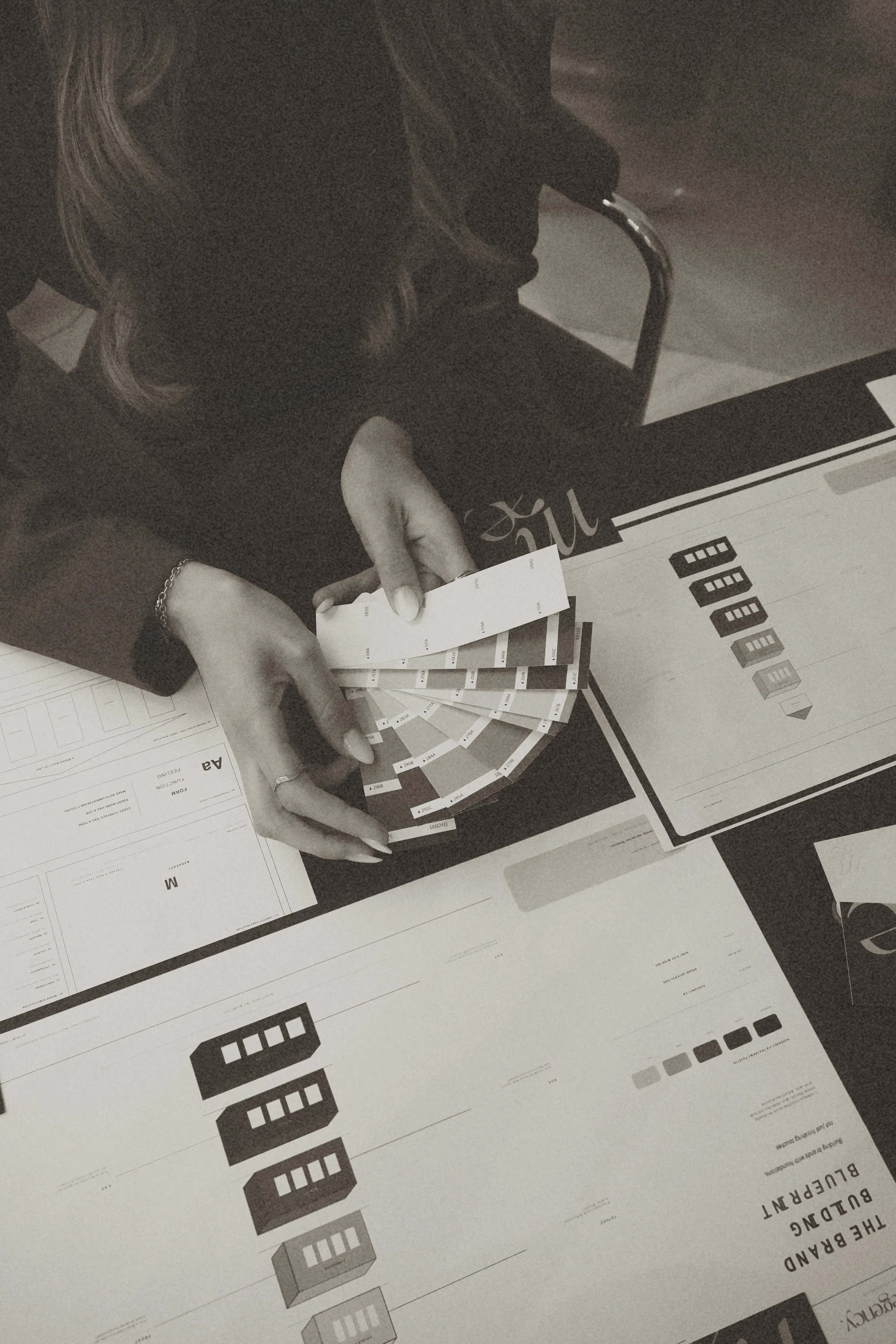 A person holding a strip of test results or color options over printed sheets and a brochure on a table.