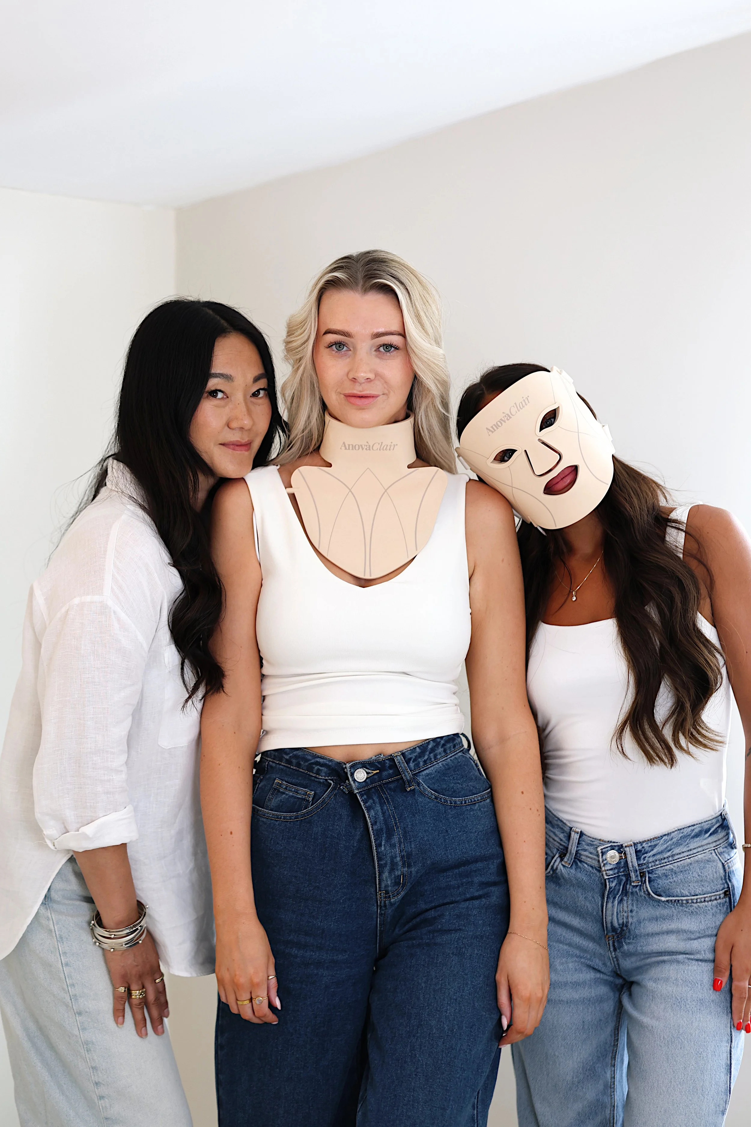 Three women standing together, one wearing a luxury mask, another with a neck brace, in front of a plain white background.