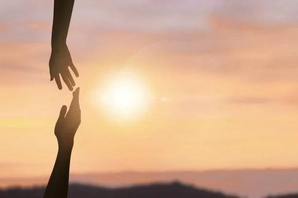 Two silhouetted hands reaching towards each other against a sunset background.