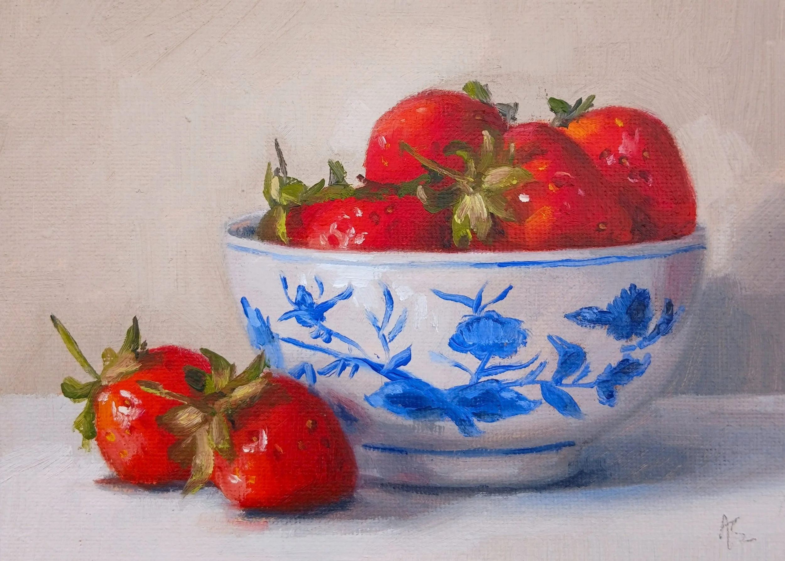 A still life oil painting of fresh strawberries in a blue and white patterned bowl with additional strawberries outside the bowl on a light-colored surface. Painted in a contemporary realist style by Artist Amanda Selway