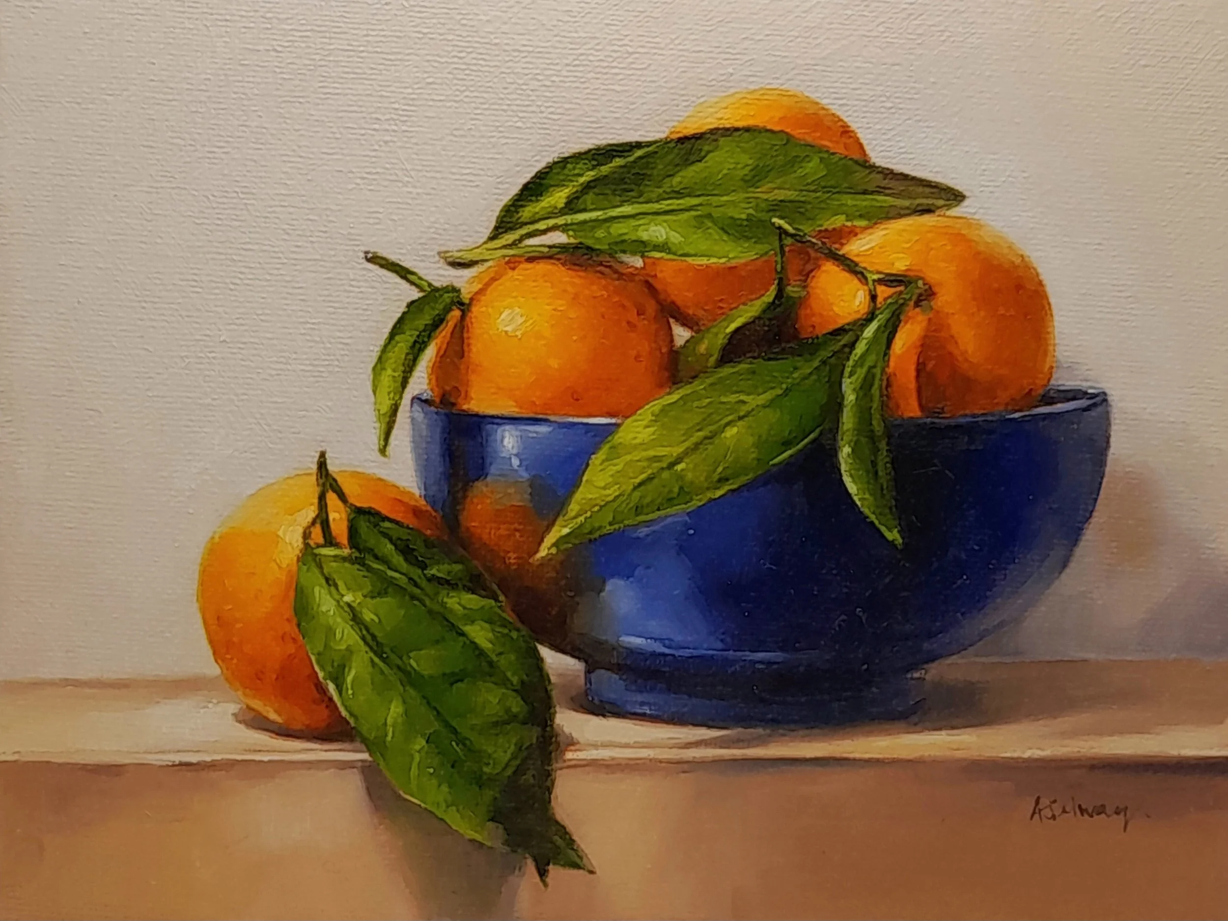 Oil painting by Amanda Selway of bright orange clementines nestled among lush green leaves in a dark blue bowl, set against a soft neutral background, in a contemporary realism style.