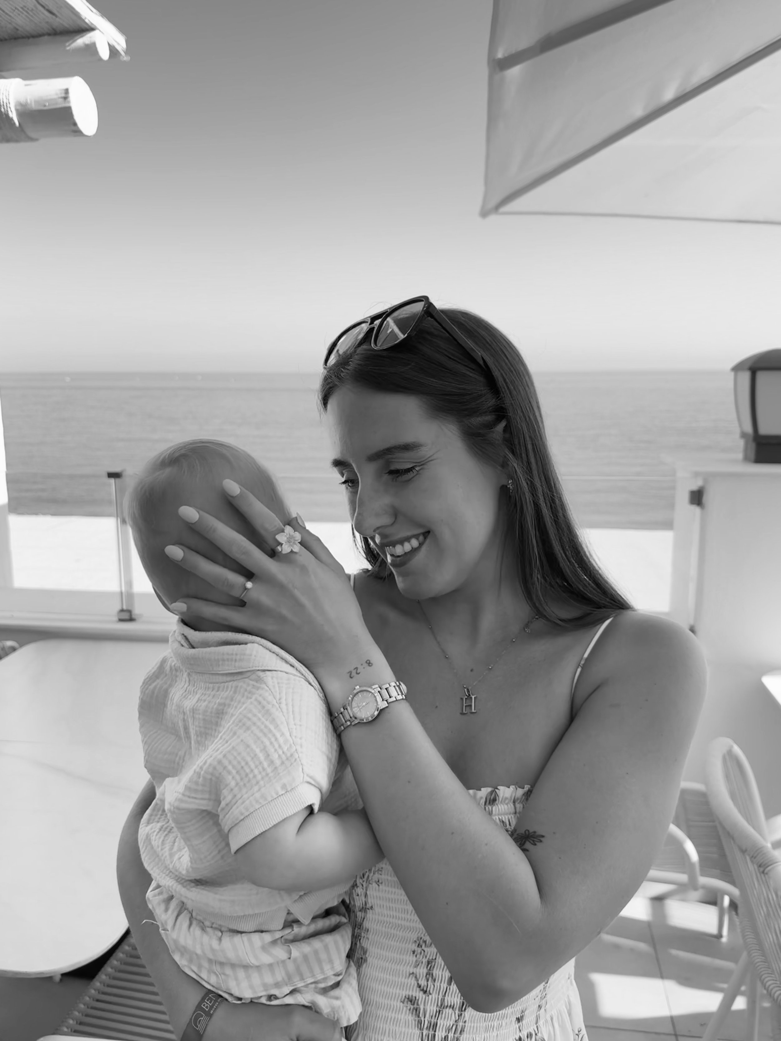 A woman holding a young child on a boat deck, smiling and sharing a close moment, with water and sky in the background, in black and white.