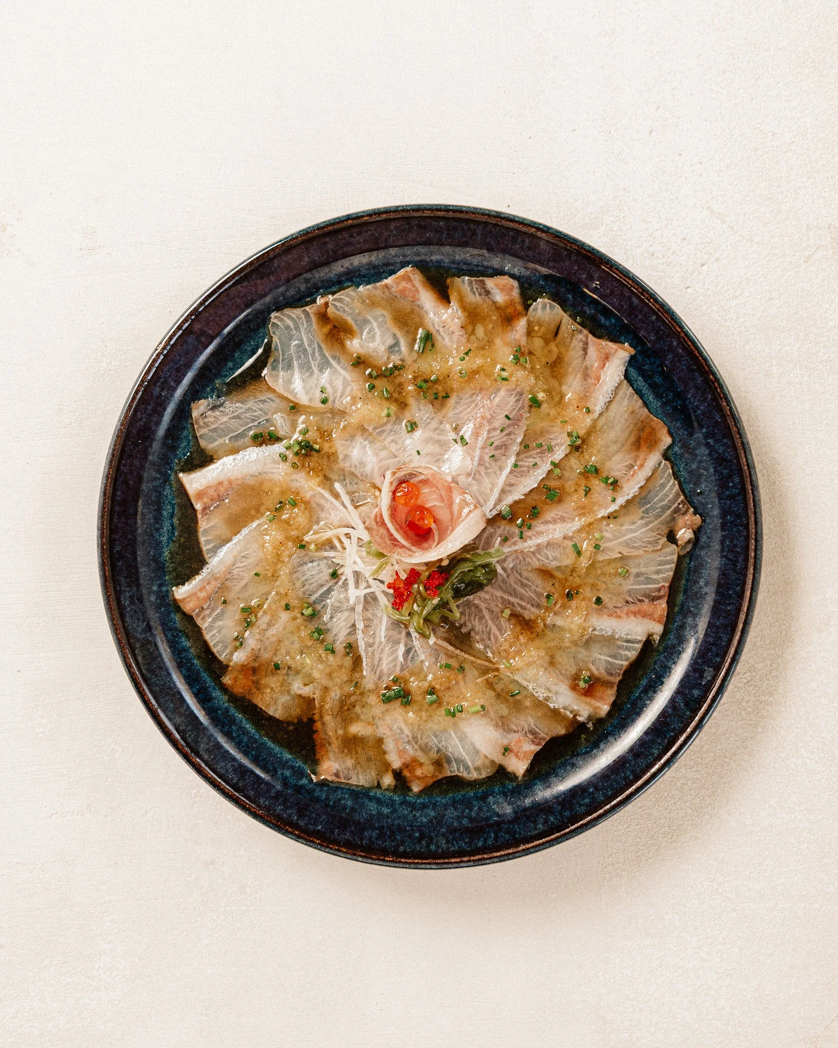 Prato de fatias de peixe branco servido com molho e decorado com cebolinhas picadas.