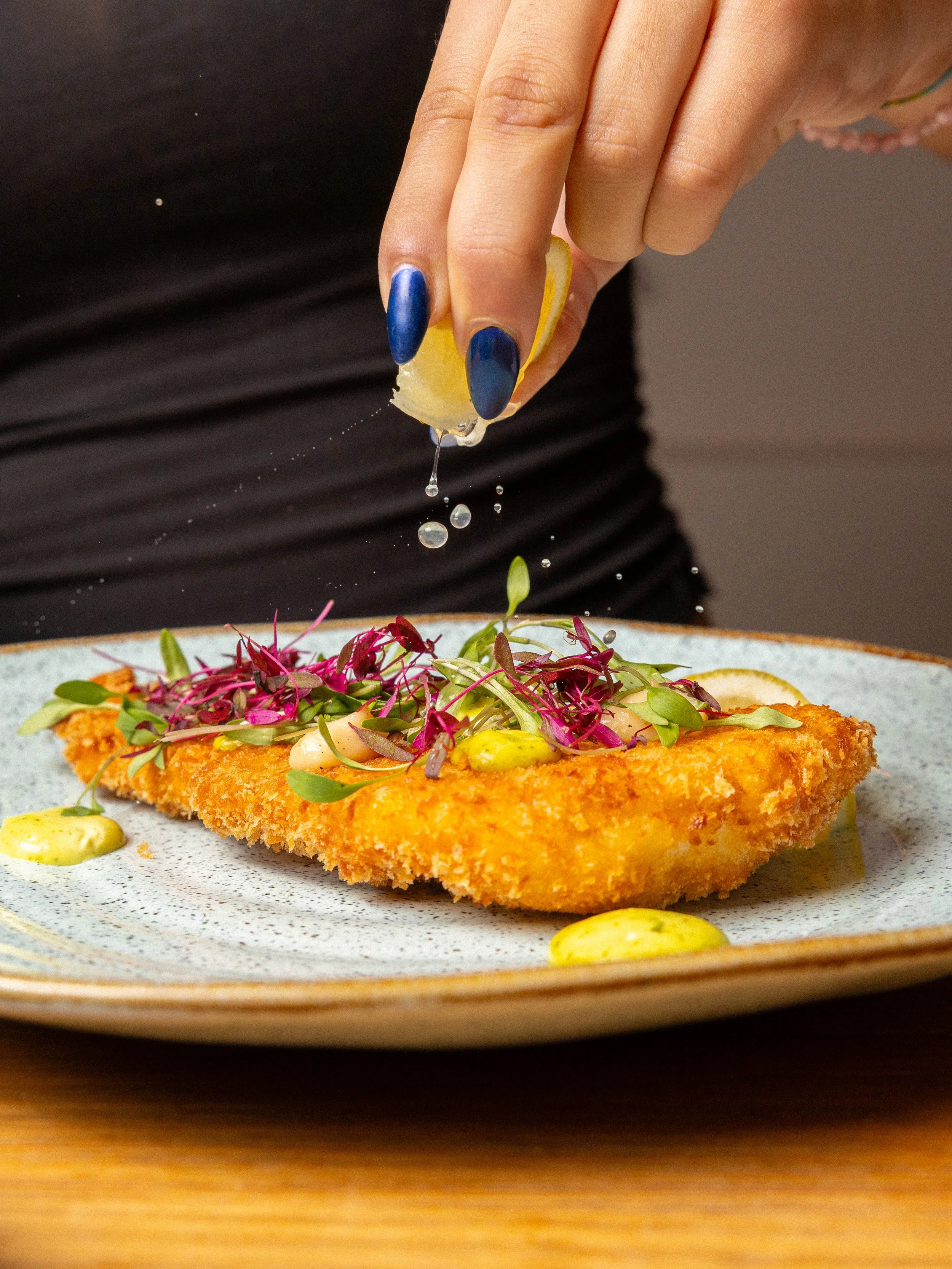 Filé de peixe empanado servido com molho de mostarda e microverdes decorativos.