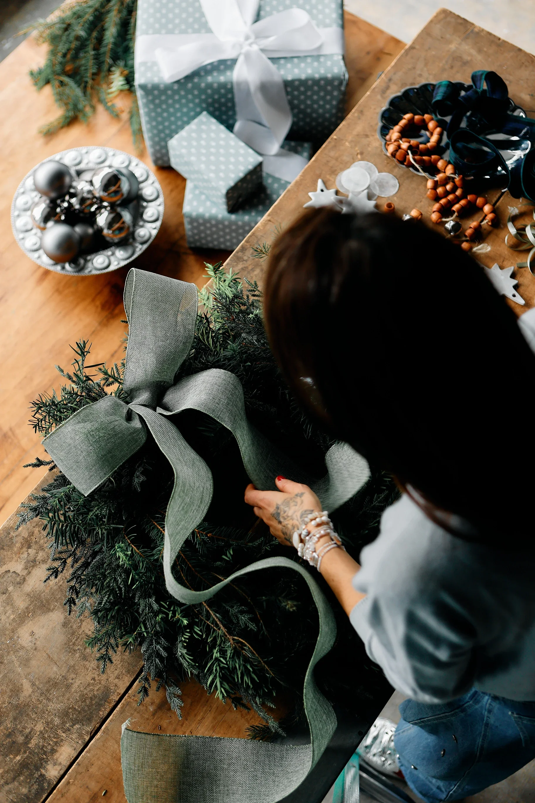 Guest tying a sage ribbon bow on a fresh evergreen wreath at Wreath Bar
