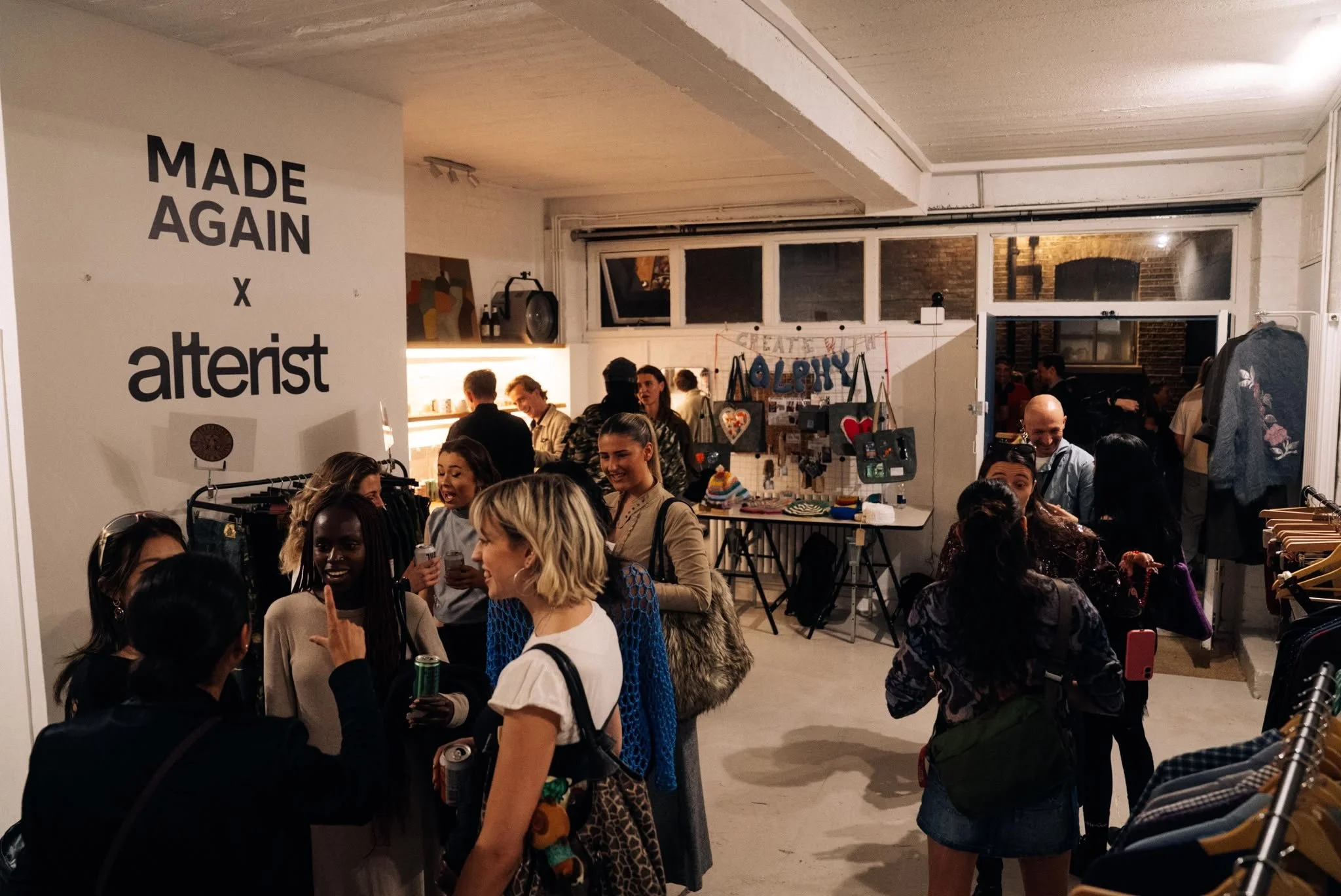 A crowded indoor market or shop with many people shopping and interacting. Walls decorated with signs, clothes, and merchandise visible.