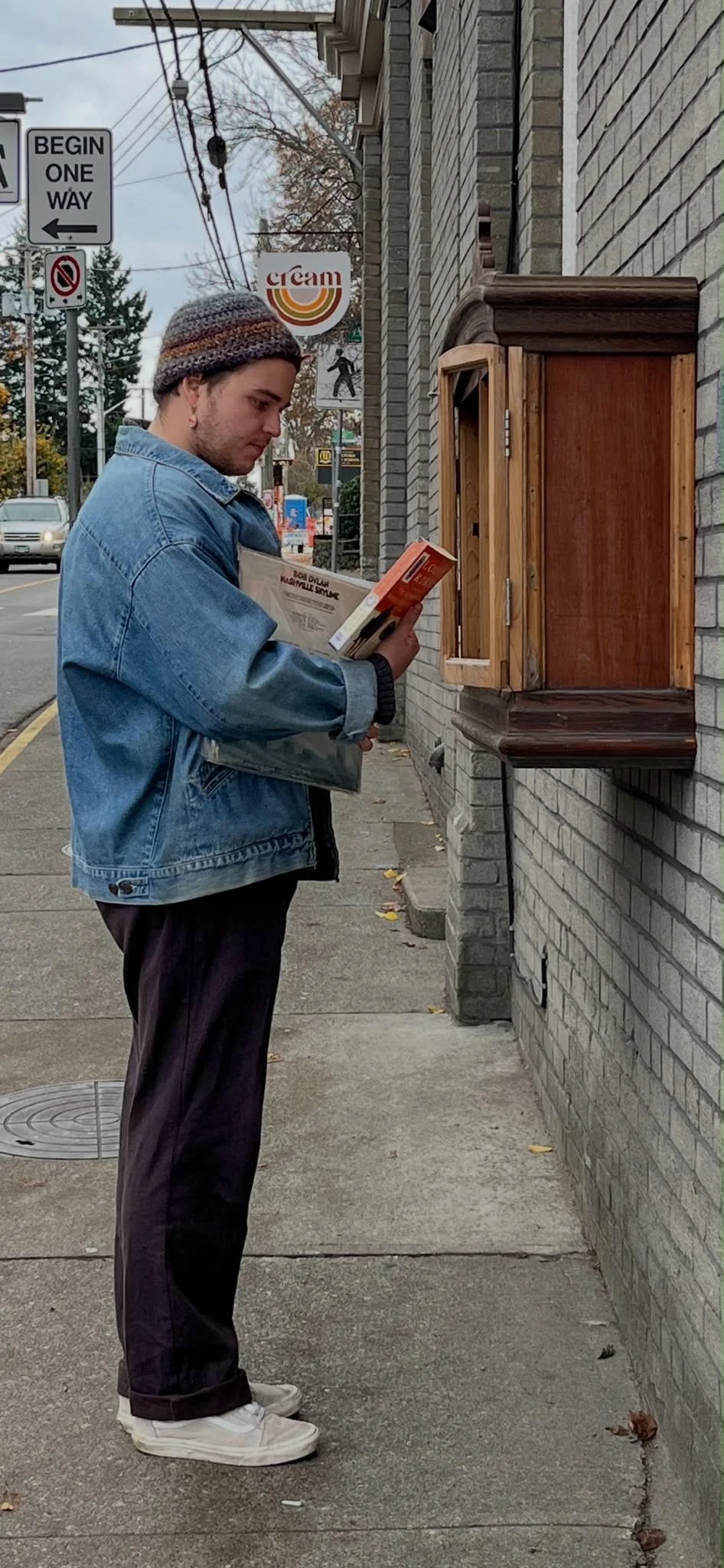 Photo of person in jean jacket in front of little library of books