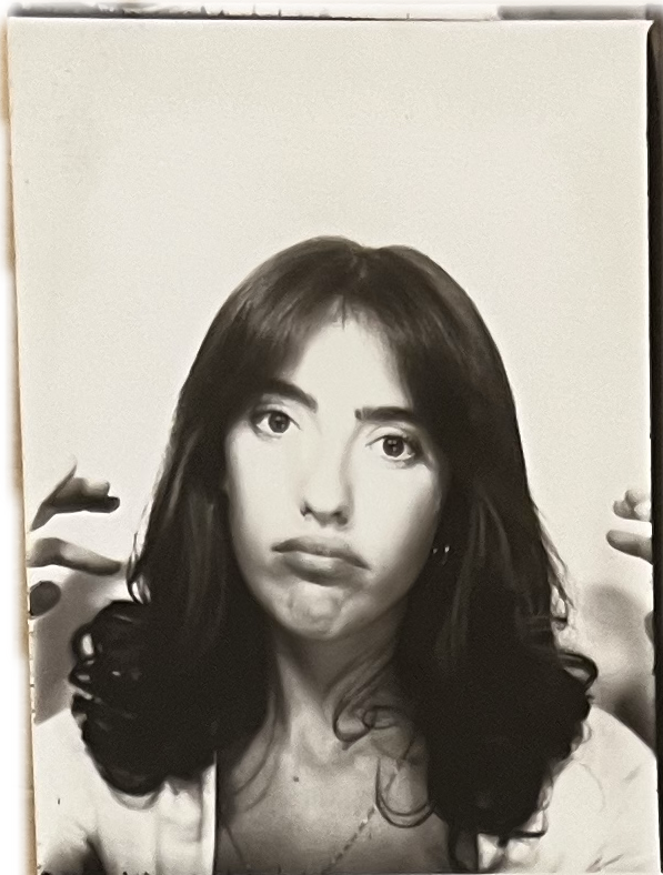 Black and white portrait of a woman with shoulder-length, wavy hair, looking directly at the camera with a neutral expression, holding her hands near her face.