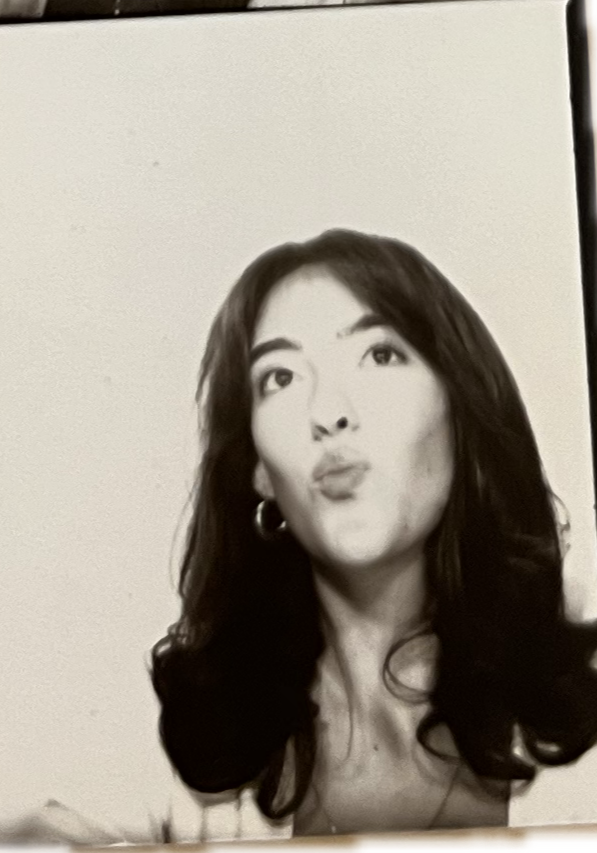 Black and white photograph of a woman with dark, wavy hair making a puckered lip expression.