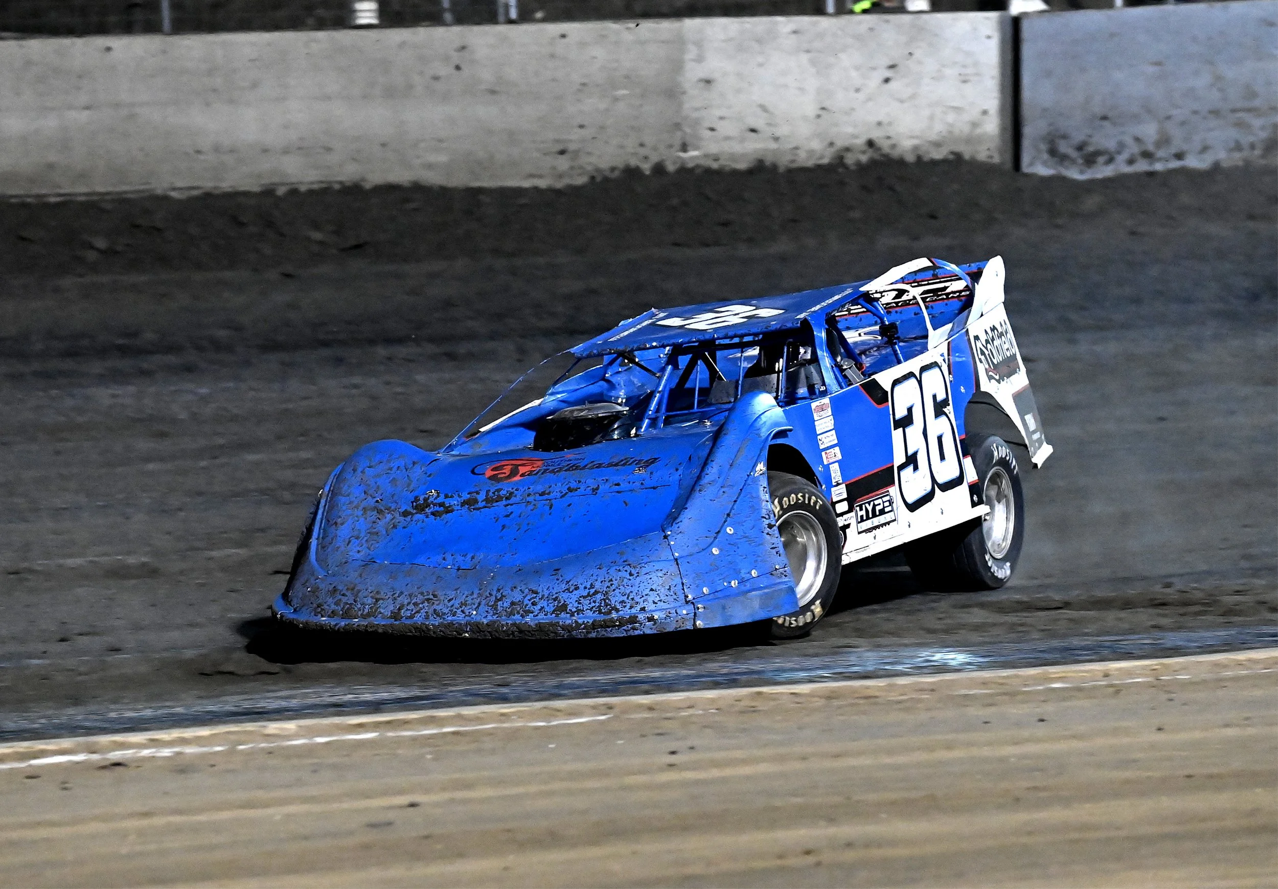 A blue race car with the number 36 on its side driving on a dirt track at night.