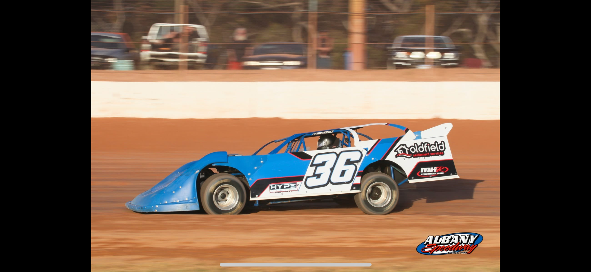 A blue racing car with the number 36 on the side speeding on a dirt race track.