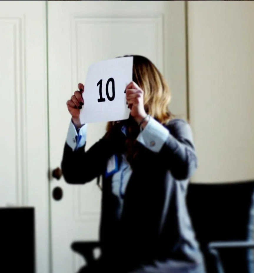 Woman in business attire holding a sign with the number 10 in front of her face.