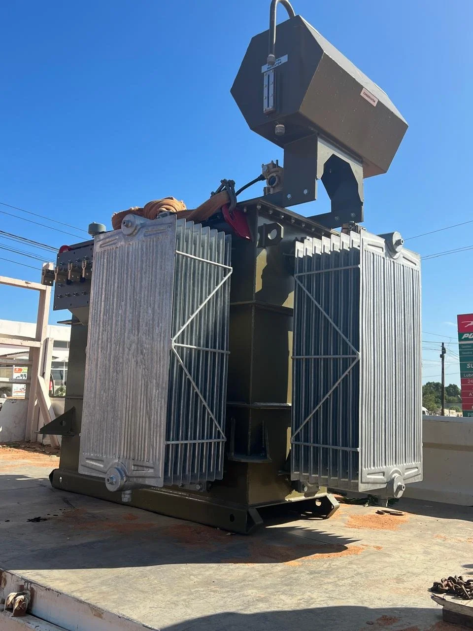 Equipamento de grande porte com componentes metálicos, possivelmente de uma máquina industrial ou de transformação, com um grande painel na parte superior sob céu claro.