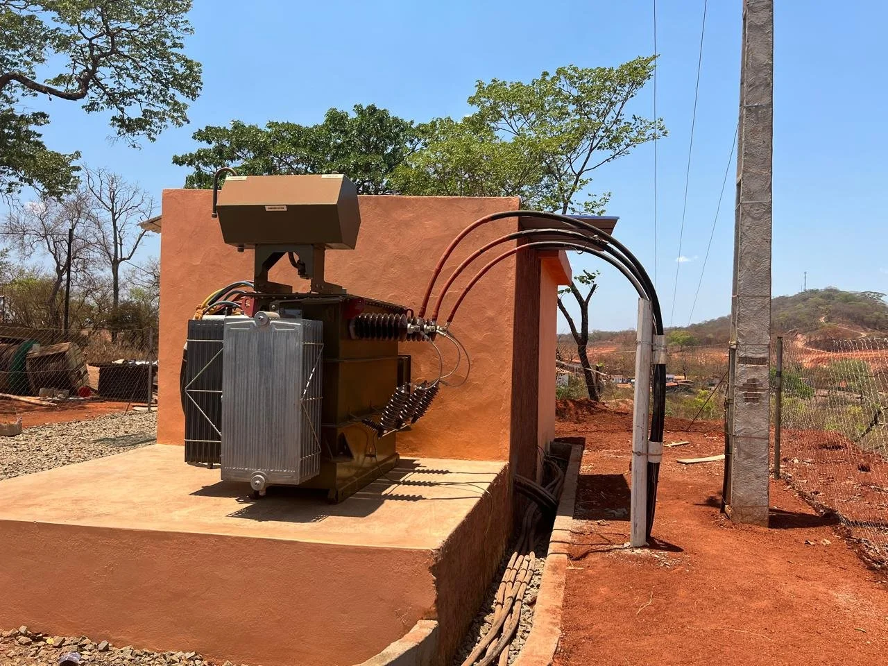 Transformador de energia elétrica ao ar livre em um terreno com árvores e céu claro.