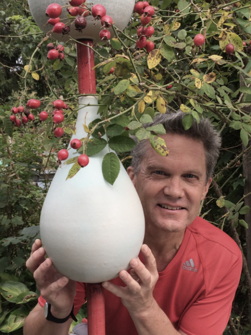 Mann hält einen weißen Keramik-Autofokus-Vase neben einem Strauch mit roten Beeren