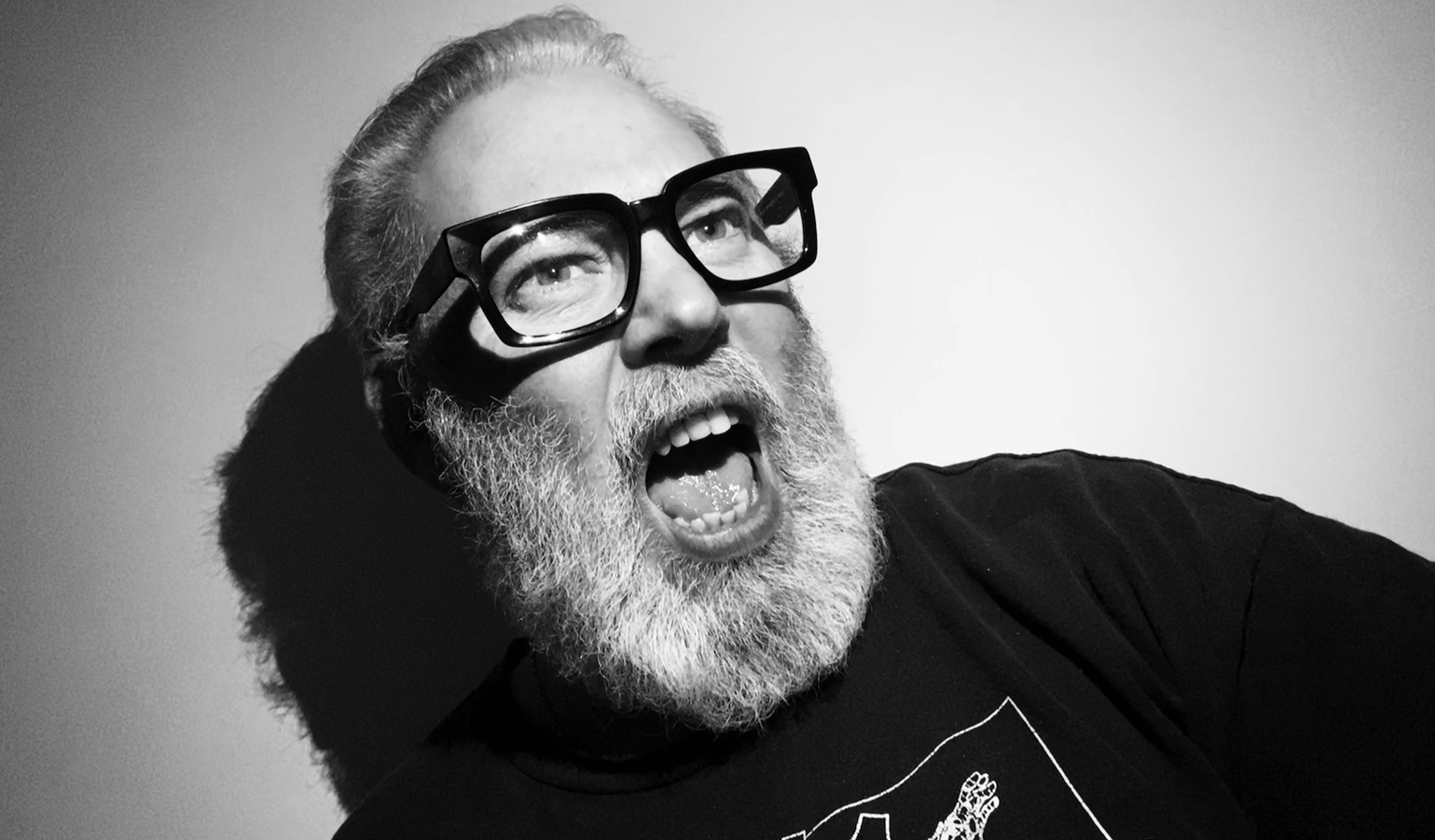 A man with a beard and glasses, expression of surprise or excitement, in black and white, against a plain background.