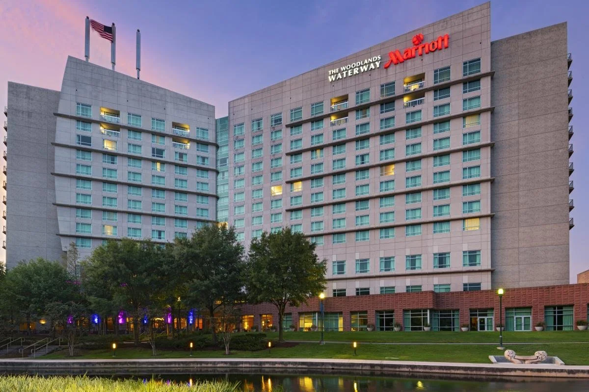 View of The Woodlands Waterway Marriott hotel with trees and water feature in the foreground during dusk.