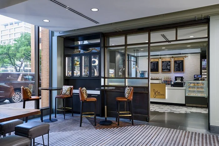 Interior of a modern cafe with seating area and a counter, window view of parked cars and city buildings outside.