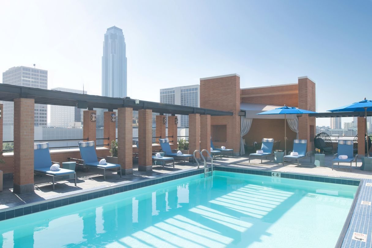 Rooftop swimming pool with lounge chairs, umbrellas, and city skyline in the background