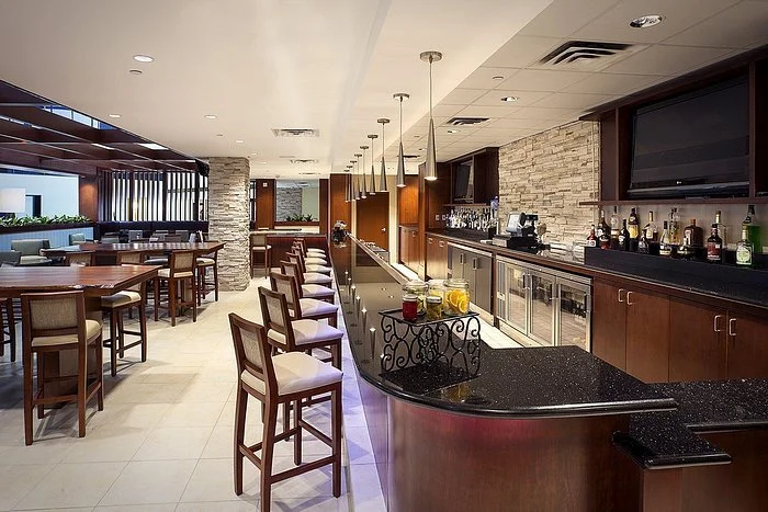 Bar area with a black granite counter, pendant lights, wooden chairs, and a television on the wall in a modern restaurant or lounge