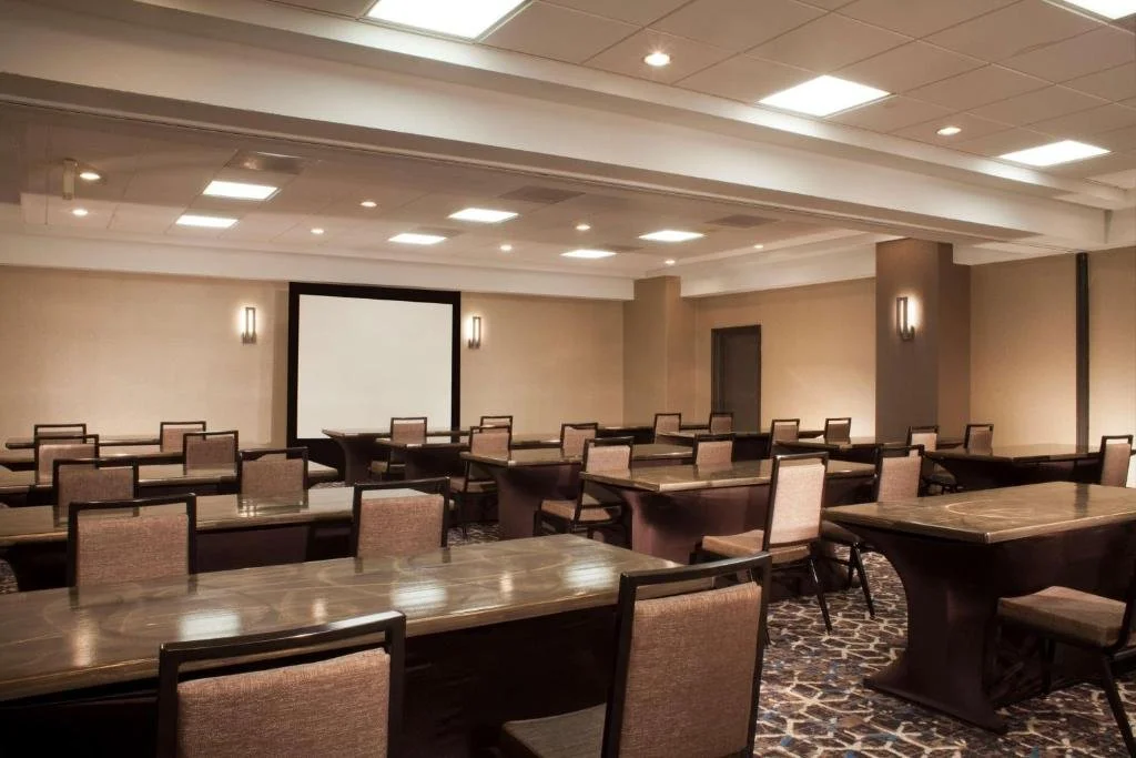 Empty conference room with rows of tables and chairs facing a large projection screen.