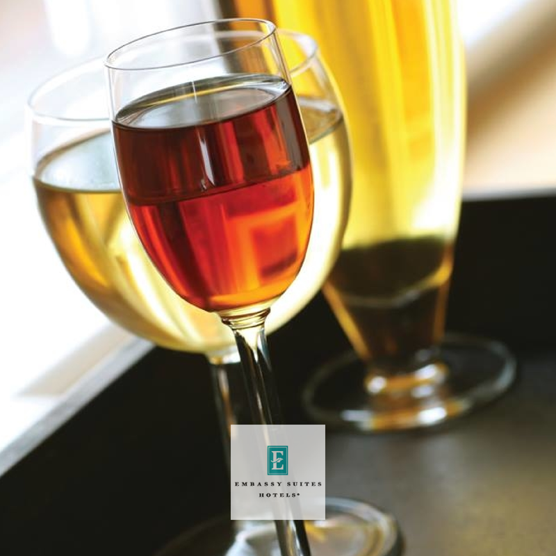 Three glasses of wine, one red and two white, on a black surface with a blurred background.