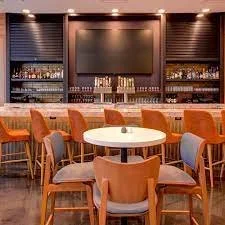 Empty bar with high chairs, white round tables, and a large blank screen on the wall.
