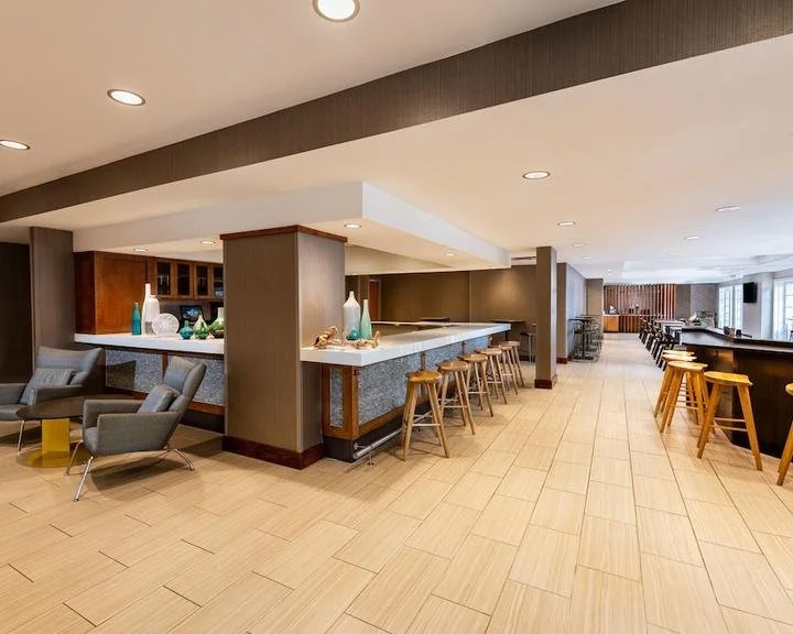 Empty hotel lounge with seating area, bar, and high tables in a modern, well-lit space.