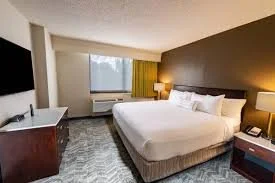 Hotel room with a large bed, bedside lamps, a window with yellow curtains, and a television in the corner.
