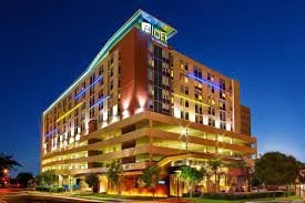 A multi-story modern hotel building with colorful exterior lighting against a darkening sky