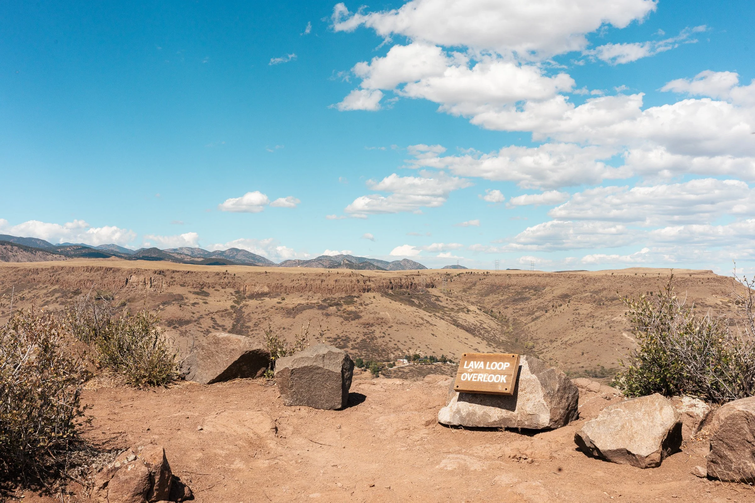 Lava Loop Overlook sign surrounded by rocks with the foothills beyond.