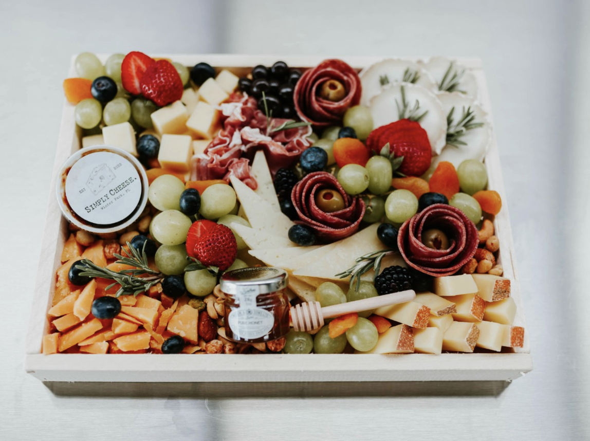 A cheese and fruit platter with grapes, strawberries, cheese, cured meats, honey, and garnishes.