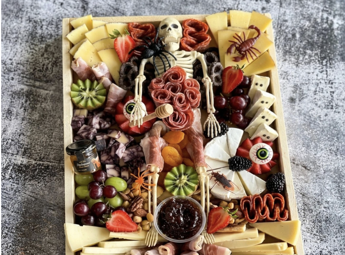 Halloween-themed charcuterie board with cheese, meats, fruits, and spooky decorations like a skeleton, spider, eyeball, and crawfish.
