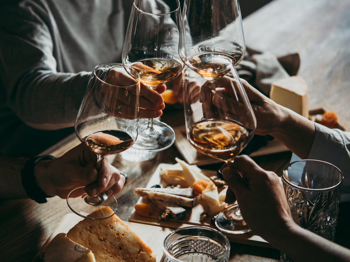 People clinking glasses of rosé wine in a toast at a cheese and charcuterie board gathering.