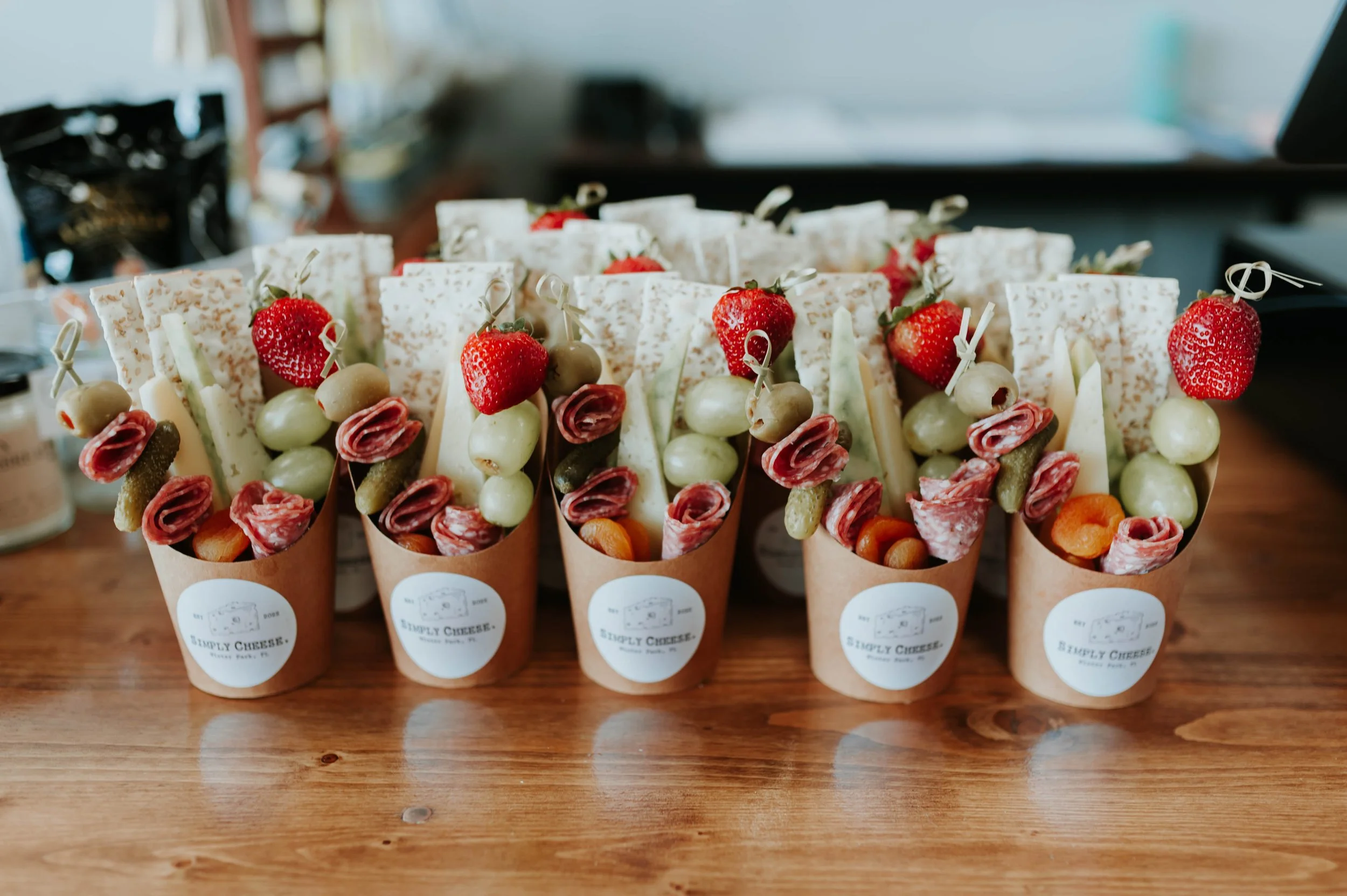 Display of multiple appetizer cones filled with assorted ingredients including grapes, strawberries, cured meat, cheese, and vegetables, labeled with a "Simply Cheese" sticker.