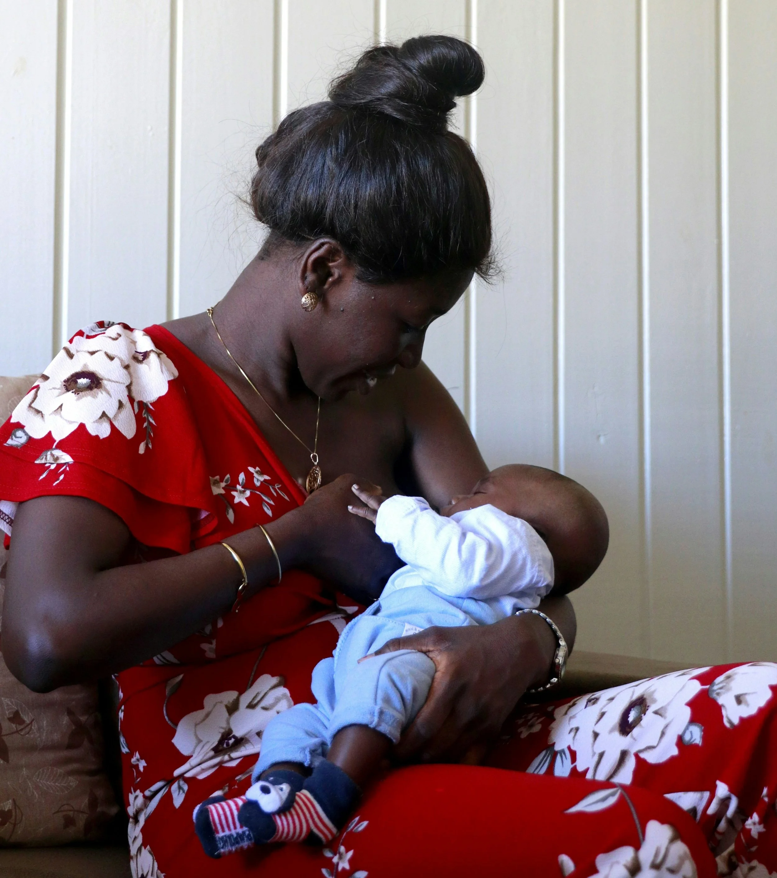 A mom in a red dress breastfeeds her baby